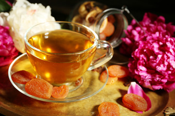Composition with cup of herbal tea, dried apricots and peony flowers on wooden background