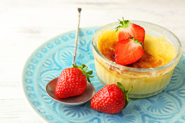 Creme brulee dessert with fresh strawberry berries on napkin, on color wooden background
