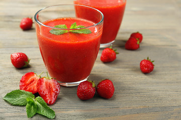 Glasses of strawberry smoothie with berries on wooden table close up
