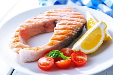 Tasty grilled salmon with tomato and lemon on table close up