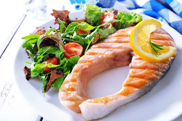 Tasty grilled salmon with salad on table close up