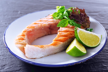Tasty grilled salmon with greens on table close up