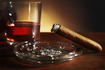 Cigars and burnt one with ash and cognac on wooden table, closeup