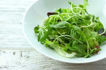 Fresh mixed green salad in bowl on wooden table close up