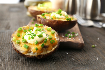 Baked potato with mayonnaise and chives on wooden cutting board, closeup