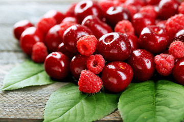 Sweet cherries, raspberries with green leaves on wooden background