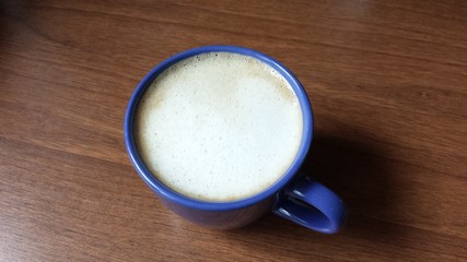 Blue cup of coffee and frothed milk on a brown counter