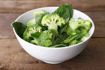 Fresh broccoli with spinach in bowl on wooden table close up