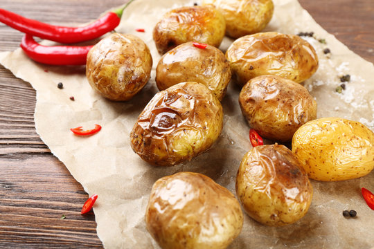 Baked spicy potatoes on parchment on wooden table, closeup