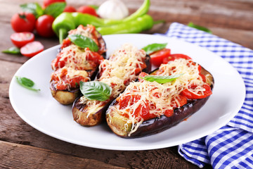 Dish of eggplant with cherry tomatoes and cheese in white plate on wooden table, closeup