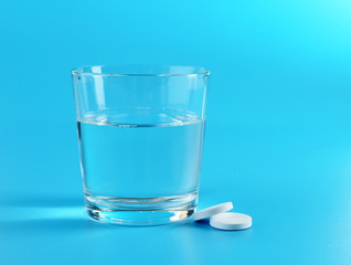 Glass of water and pills on blue background