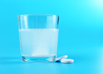 Glass of water and pills on blue background