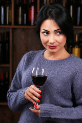 Pretty young woman with wineglass on wine shelf background