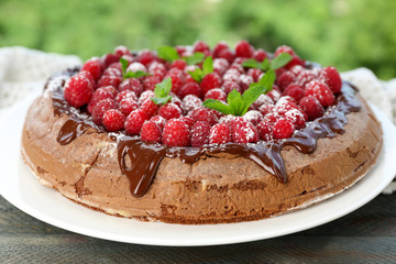 Cake with Chocolate Glaze and raspberries on wooden table, on bright background