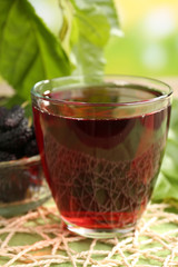 Glass of refreshing mulberry juice with berries on bright background