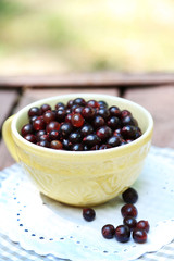 Red gooseberry in cup on wooden table close-up outdoors