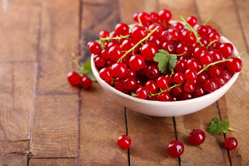 Fresh red currants in bowl on wooden table close up