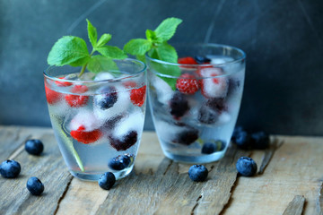 Glasses of cold refreshing summer drink with berries and ice cubes on table close up