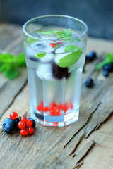 Glass of cold refreshing summer drink with berries and ice cubes on table close up
