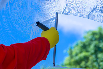 Hand cleaning window with blue sky and white clouds