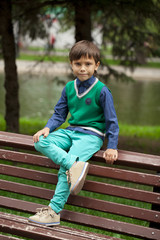 Little boy sitting on a bench in a summer park