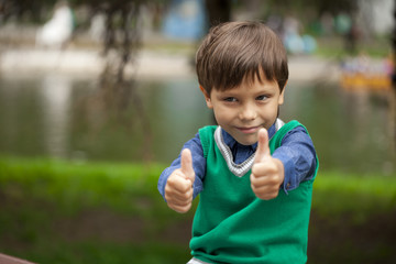 Boy with thumbs up on background summer park