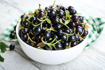 Ripe black currants in bowl on wooden table with checkered napkin, closeup