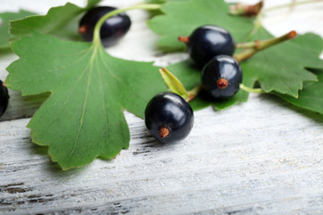Ripe black currants with green leaves on wooden background