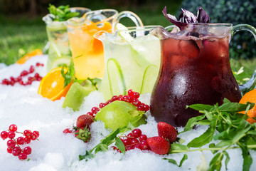 a mix of several bright colored delicious cold lemonade carafes of cucumber and orange and basilon...