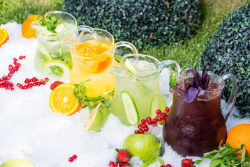 a mix of several bright colored delicious cold lemonade carafes of cucumber and orange and basilon with creative composition