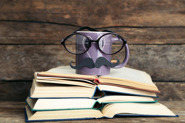 Vintage books and cup with mustache on wooden background