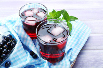 Glasses of fresh blackcurrant juice with ice cubes on checkered napkin on wooden table, closeup
