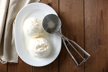 Delicious vanilla ice cream on plate, on wooden background