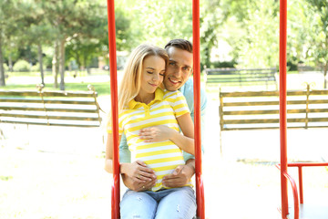 Young pregnant woman with husband on swing outdoors