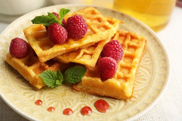 Sweet homemade waffles with fresh raspberries on plate, on light background