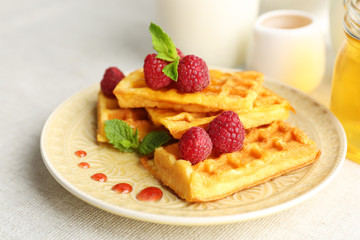 Sweet homemade waffles with fresh raspberries on plate, on light background