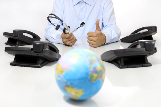 global international support concept, headset and office phone on desk with globe map