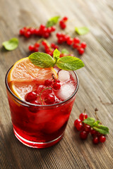 Glass of red currants juice with lemon and ice cubes on wooden table, closeup