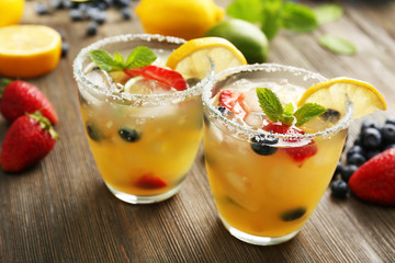 Glasses of berries juice with lemon on wooden table, closeup