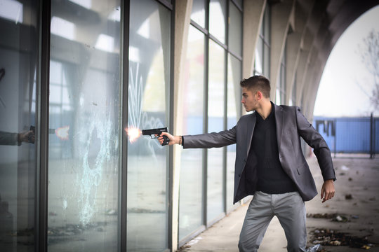 Young detective or policeman or mobster firing a gun to a window glass