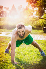 Sports man with brown hair and a beard on a natural background, performing push-ups on one arm