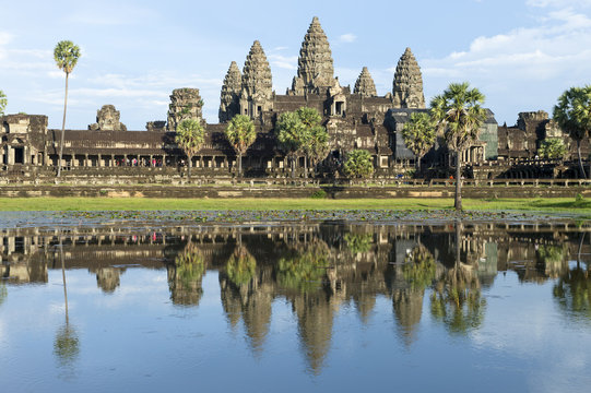 Ancient temple complex of Angkor Wat reflecting in still water under blue sky