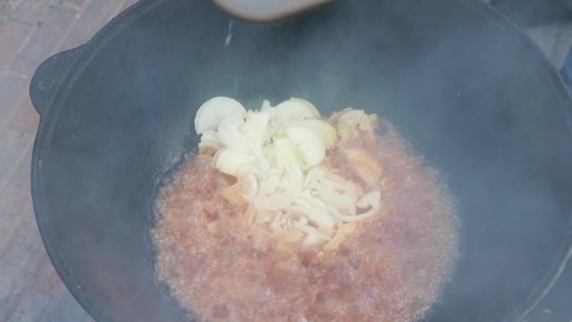 Uzbek national dish pilaf in a large cast-iron cauldron on the fire, fry the chopped onion until golden brown, lamb, carrot, mutton fat, the fat tail, sesame oil, garlic