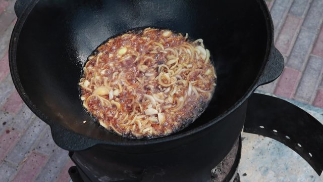 Uzbek national dish pilaf in a large cast-iron cauldron on the fire, fry the chopped onion until golden brown, lamb, carrot, mutton fat, the fat tail, sesame oil, garlic
