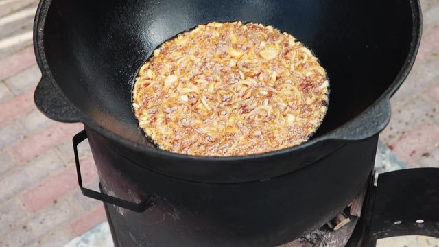 Uzbek national dish pilaf in a large cast-iron cauldron on the fire, fry the chopped onion until golden brown, lamb, carrot, mutton fat, the fat tail, sesame oil, garlic