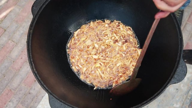 Uzbek national dish pilaf in a large cast-iron cauldron on the fire, fry the chopped onion until golden brown, lamb, carrot, mutton fat, the fat tail, sesame oil, garlic