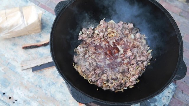 Uzbek national dish pilaf in a large cast-iron cauldron on the fire, add the lamb pieces and stir fry, rice, carrot, mutton fat, the fat tail, sesame oil, onion, garlic, red hot chili pepper