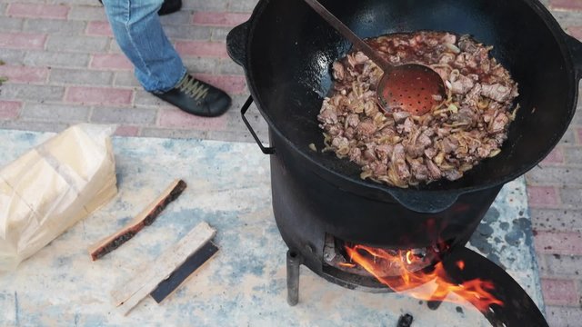 Uzbek national dish pilaf in a large cast-iron cauldron on the fire, add the lamb pieces and stir fry, rice, carrot, mutton fat, the fat tail, sesame oil, onion, garlic, red hot chili pepper