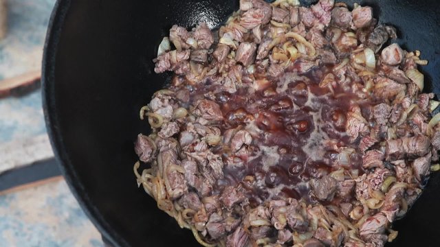 Uzbek national dish pilaf in a large cast-iron cauldron on the fire, add the lamb pieces and stir fry, rice, carrot, mutton fat, the fat tail, sesame oil, onion, garlic, red hot chili pepper