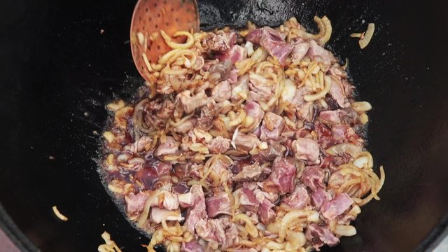 Uzbek national dish pilaf in a large cast-iron cauldron on the fire, add the lamb pieces and stir fry, rice, carrot, mutton fat, the fat tail, sesame oil, onion, garlic, red hot chili pepper